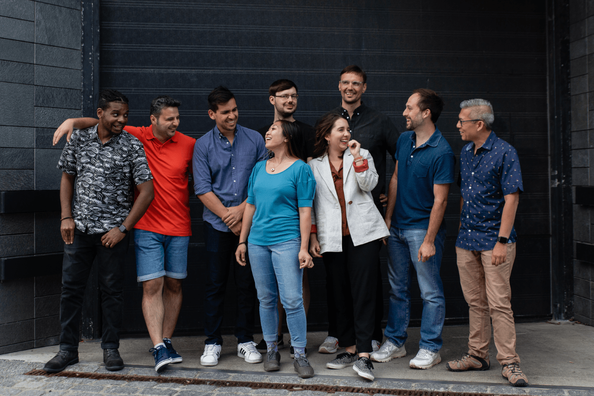 The Stately team including Gavin, Farzad, David, Mateusz, Jenny, Laura, Anders, Nick, and Kevin, all standing in front of garage doors, laughing and smiling at each other.